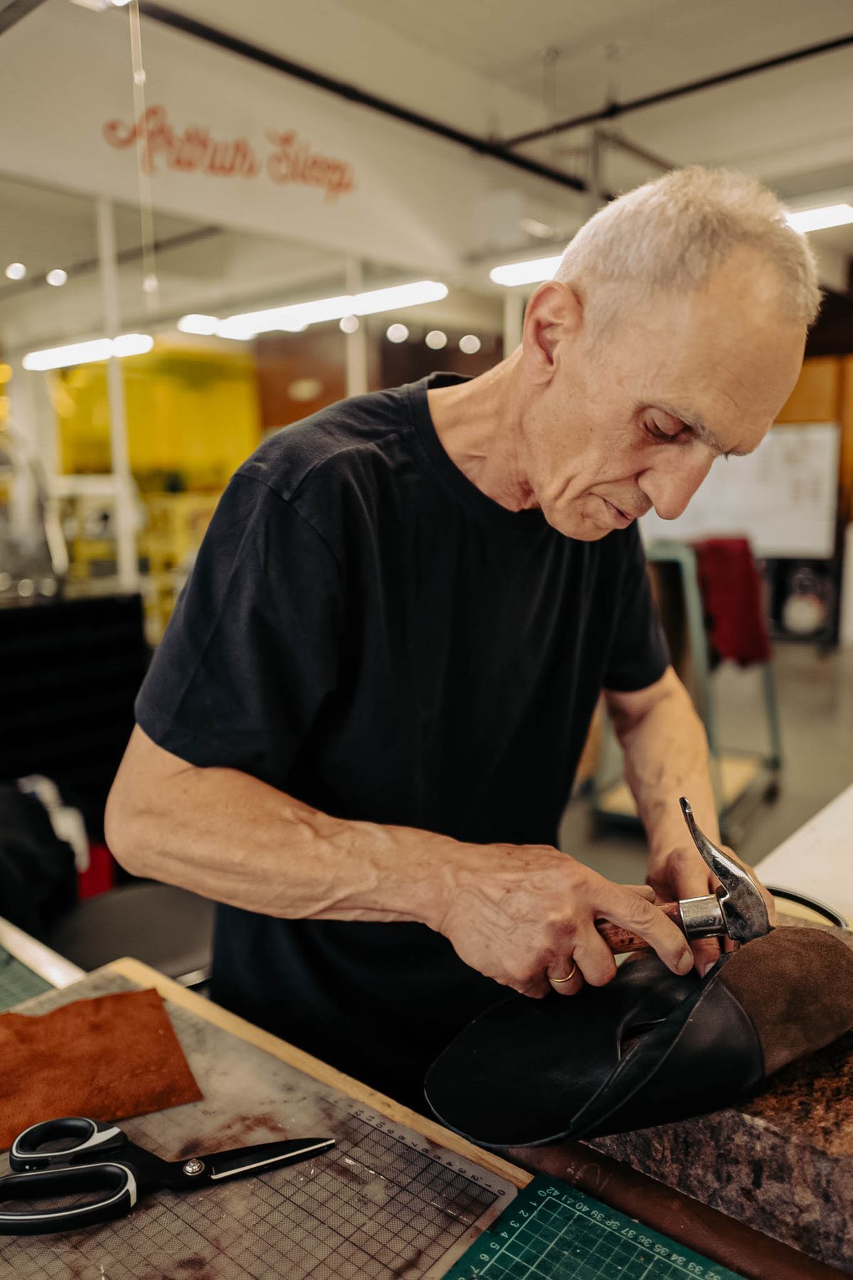 A maker at the bench in our factory, working a shoe with a lasting hammer