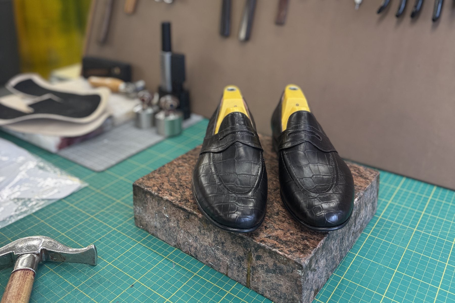 Black crocodile penny loafers on a granite block at a bench in our workshop, tools hanging behind